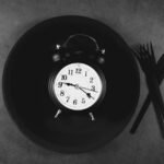 Alarm clock on an empty plate with a knife and fork, representing meal timing