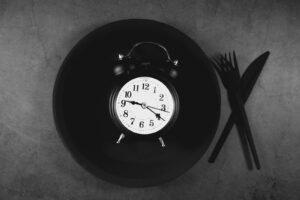 Alarm clock on an empty plate with a knife and fork, representing meal timing
