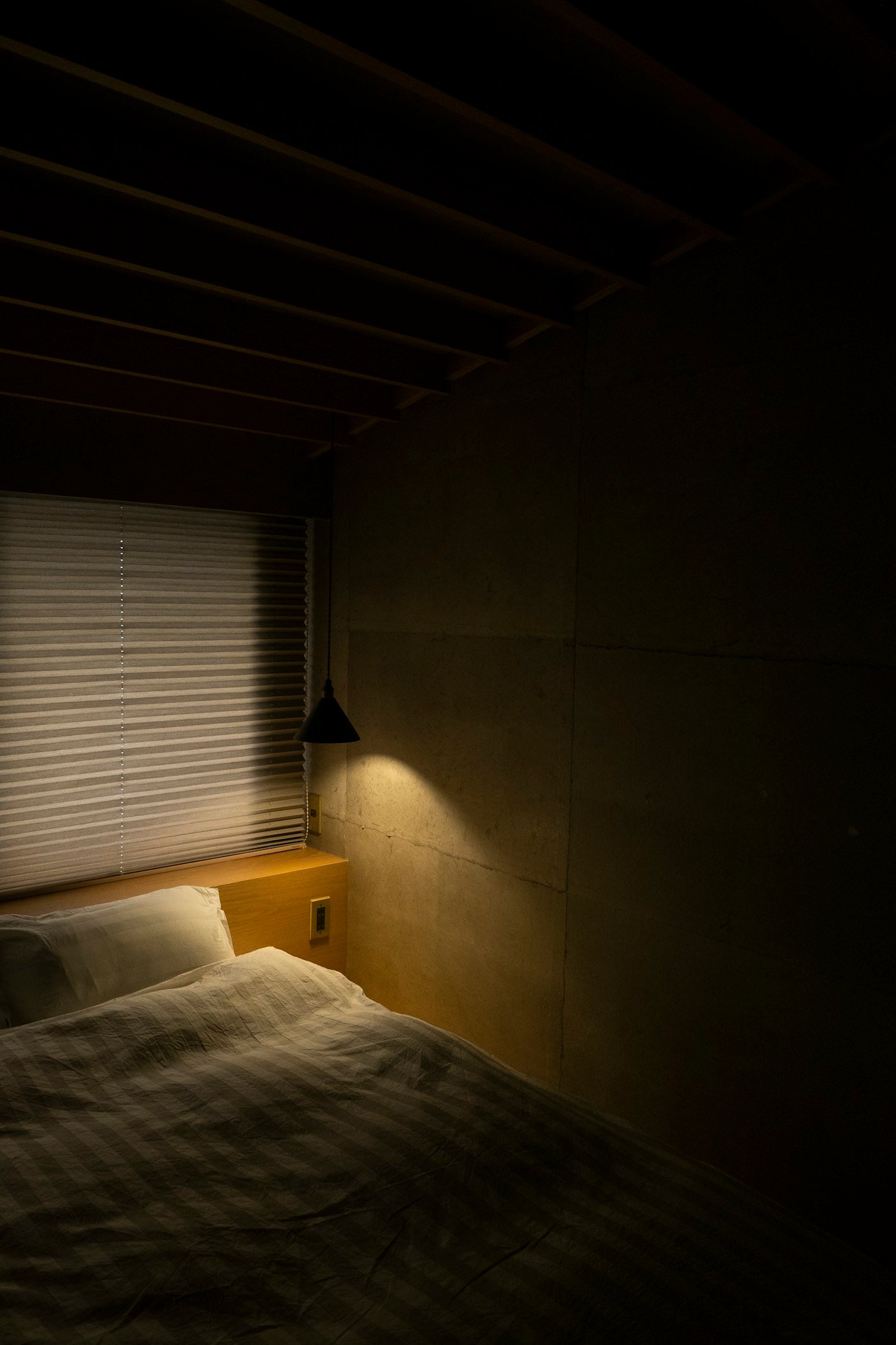 White bed linen beside a window with morning light coming through the blinds