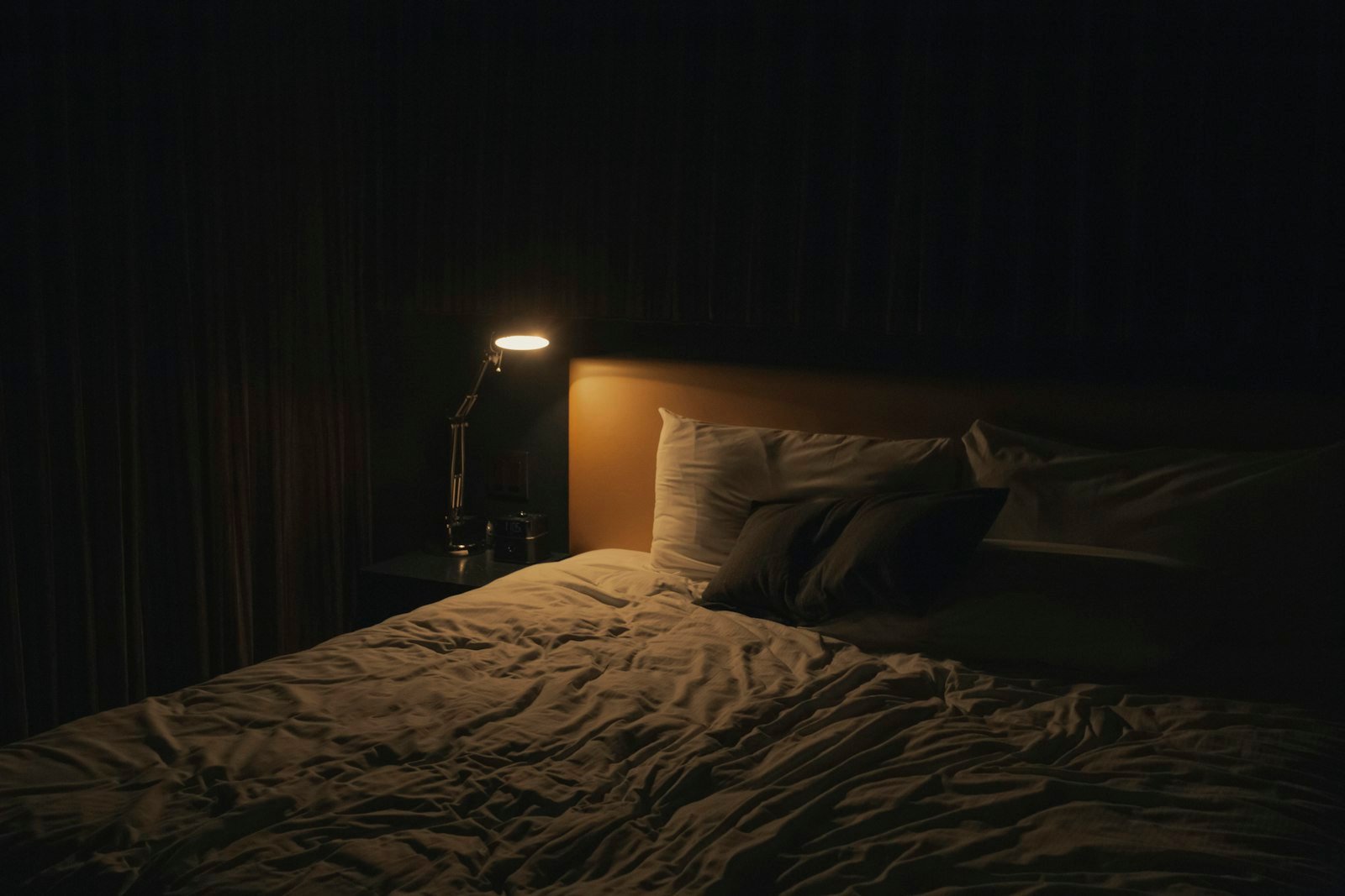 A warm table lamp glowing beside a bed in the evening
