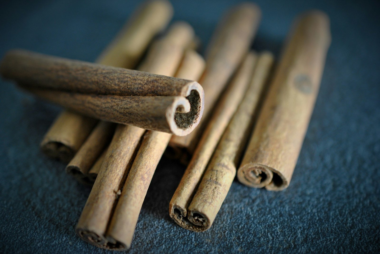 A pile of cinnamon sticks on a dark surface