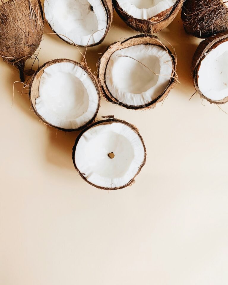 Halved and whole coconuts on a white surface