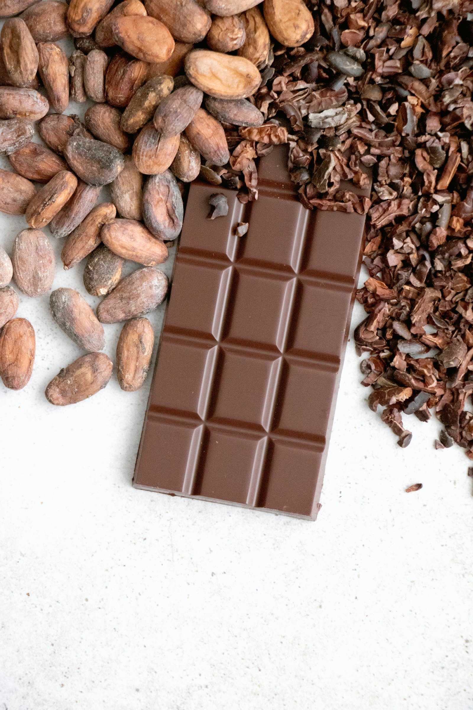 A bar of dark chocolate next to a pile of nuts