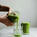 Person holding a clear glass of green vegetable juice