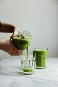 Person holding a clear glass of green vegetable juice