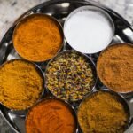 Various colorful kitchen spices arranged in metal bowls on a tray
