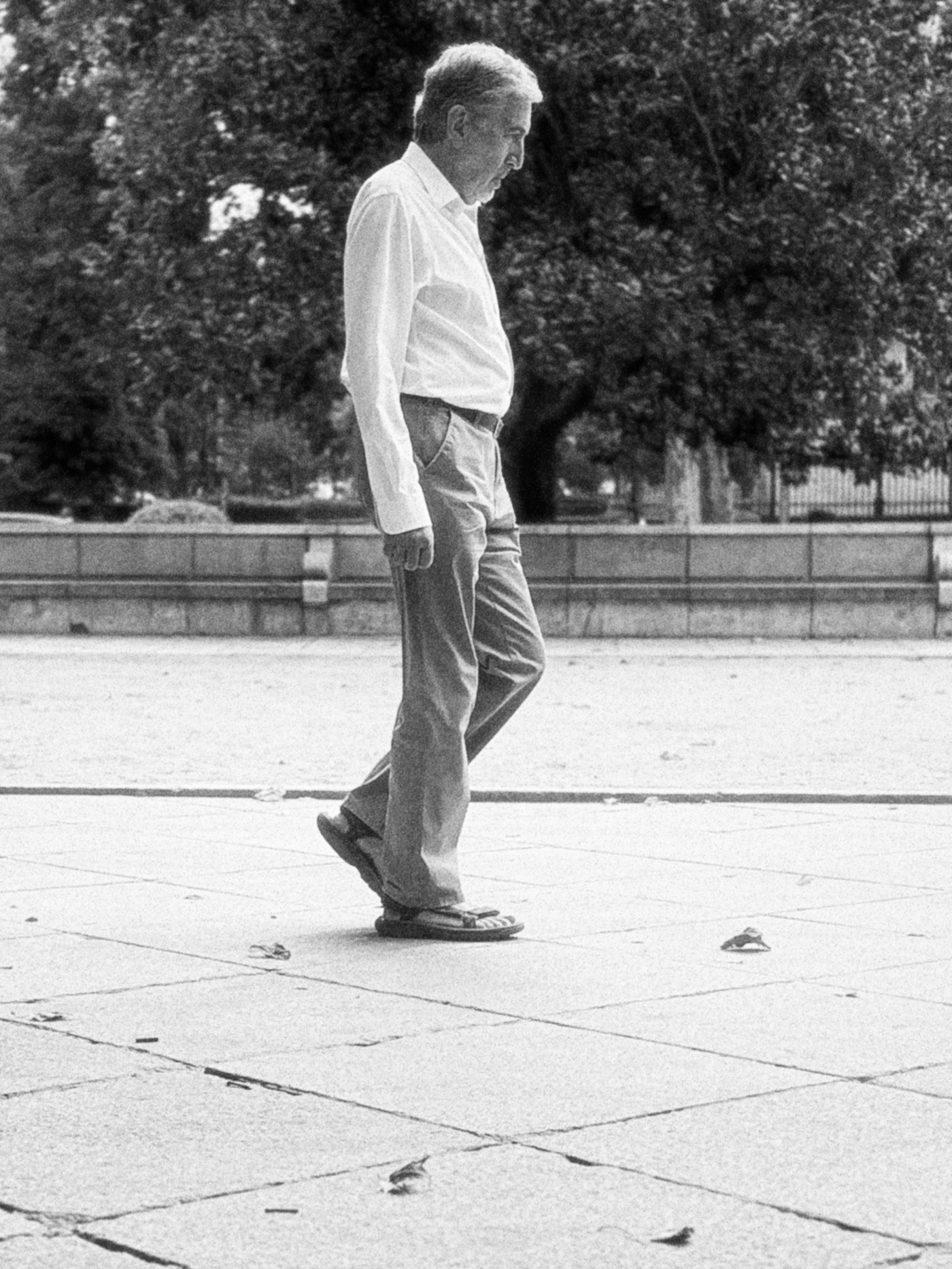 Older man in a white shirt taking a brisk walk across a paved plaza