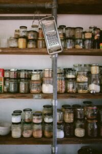 Assorted glass jars of grains, beans, and seeds on a white wooden shelf