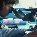 Scientist in a white lab coat looking through a microscope in a laboratory
