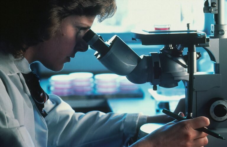 Scientist in a white lab coat looking through a microscope in a laboratory