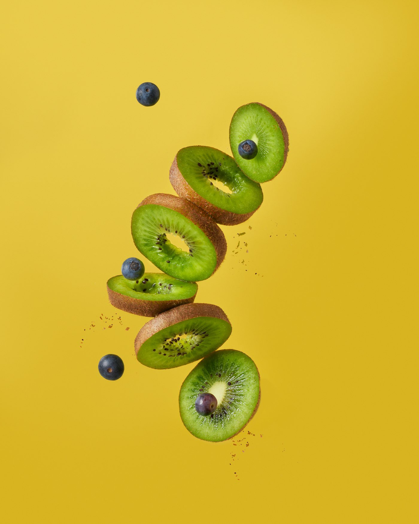 Whole fuzzy brown kiwis and halved green kiwifruit on a blue surface