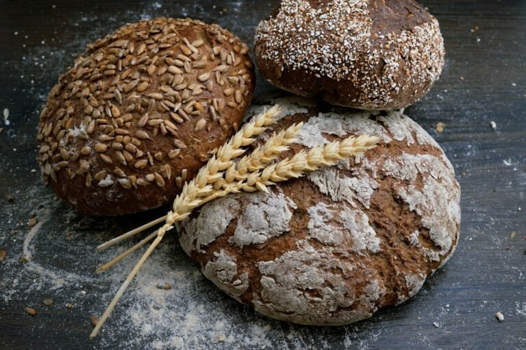 Three loaves of rustic whole grain bread with sunflower seeds and wheat stalks on wood