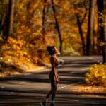 Woman in athletic wear running on a road lined with autumn trees