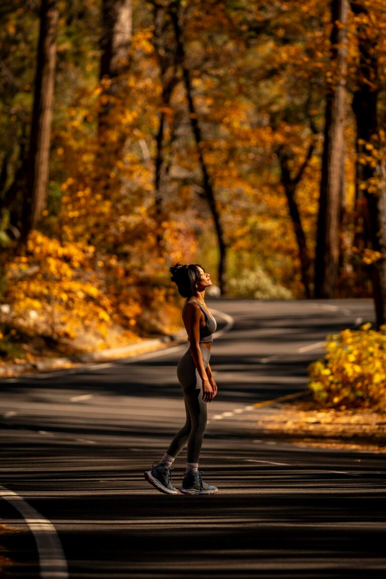 Woman in athletic wear running on a road lined with autumn trees