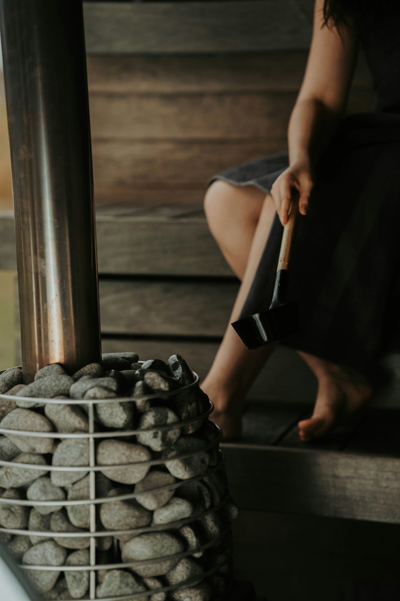Woman sitting on a sauna bench next to a stove filled with hot stones